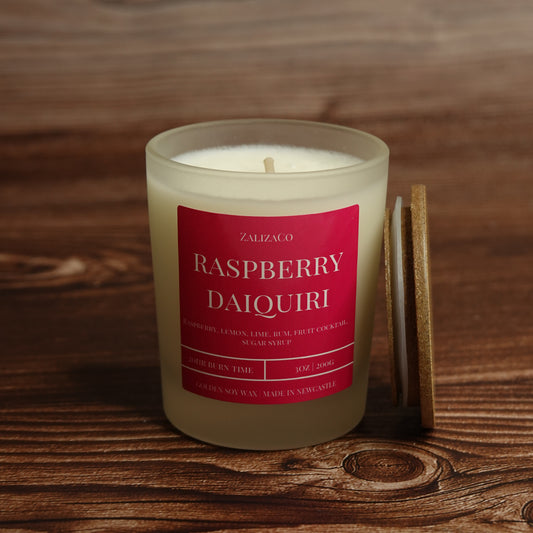 A Zalizco Raspberry Daiquiri scented soy candle in a frosted glass jar, shown on a rustic wooden surface next to its wooden lid.